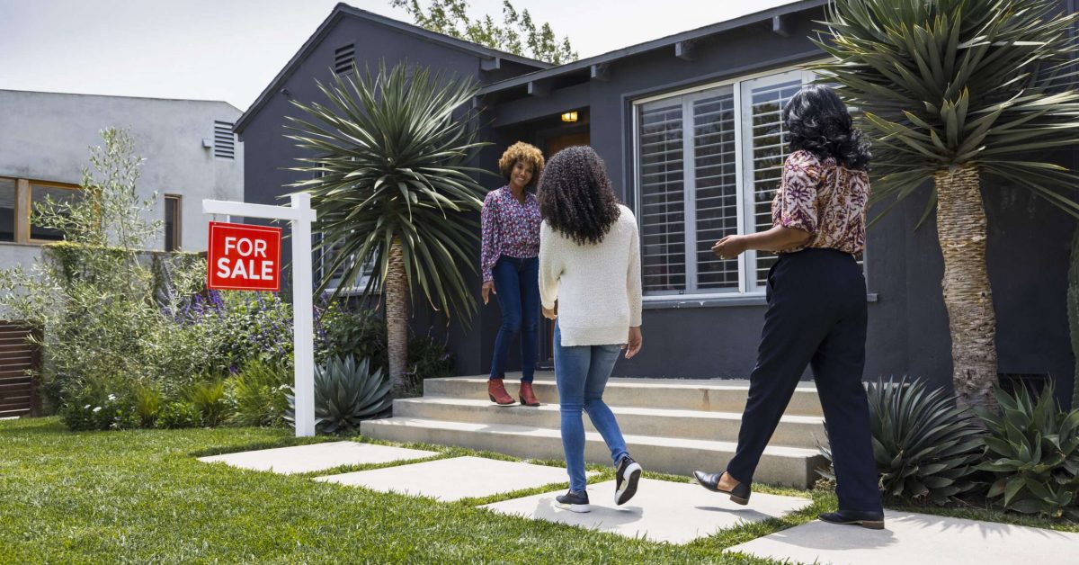 Full length of saleswoman greeting female customers while standing outside house