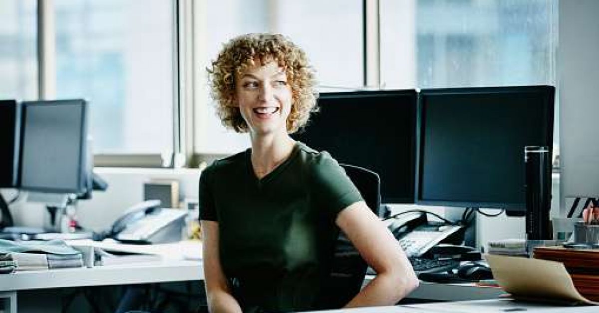 Smiling businesswoman in discussion with coworker at office workstation